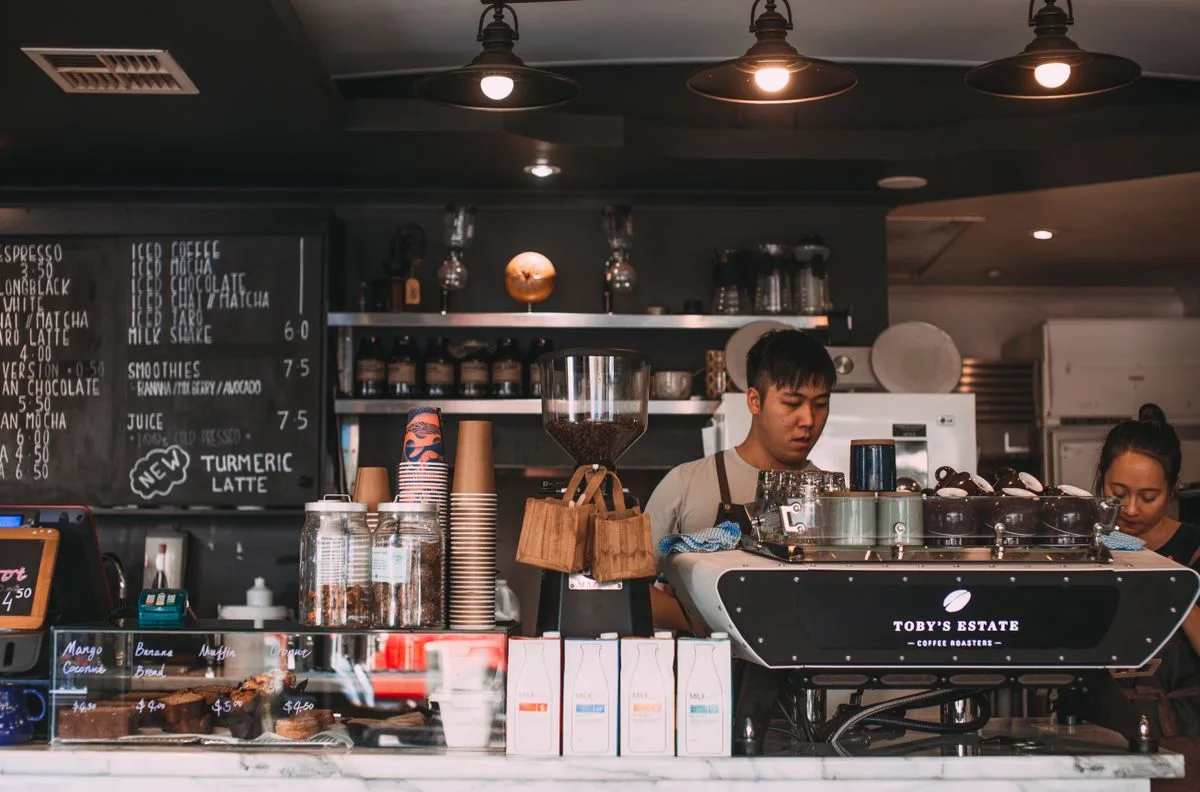 Baristas working at a café counter with stacks of takeaway cups