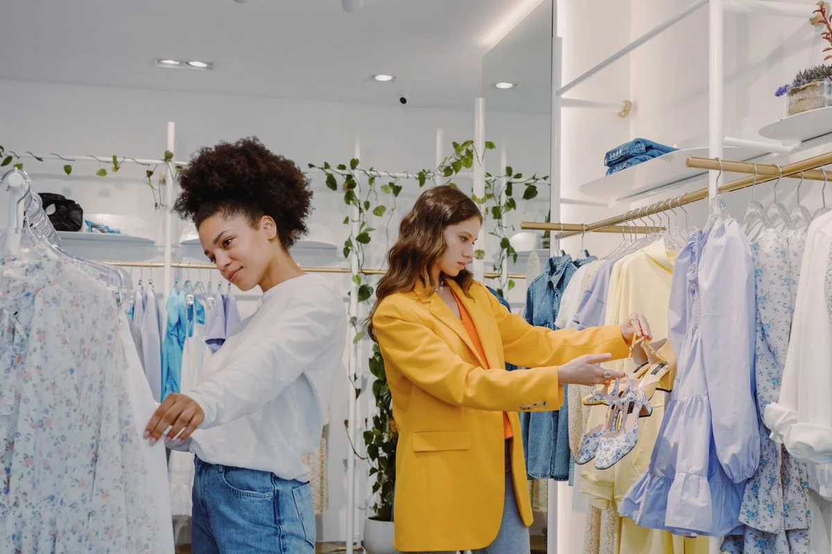 Two shoppers browsing outfits in a bright boutique